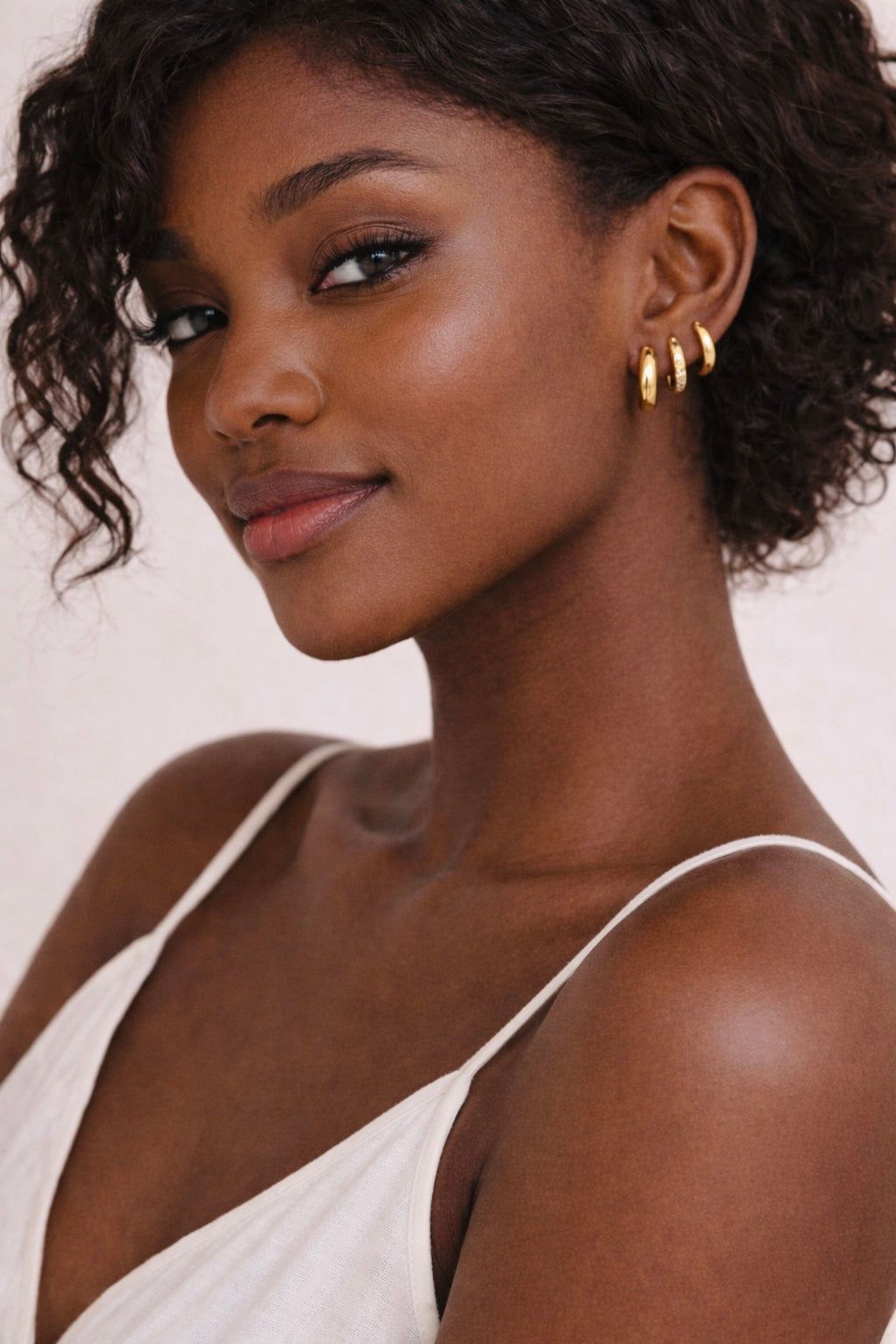 Model wearing Luma Huggies non-tarnish waterproof gold hoop earrings in stainless steel for everyday luxury styling.